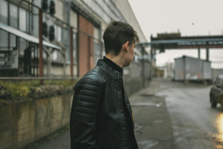 homme vêtu d'une veste en cuir noir debout sur le trottoir pendant la journée